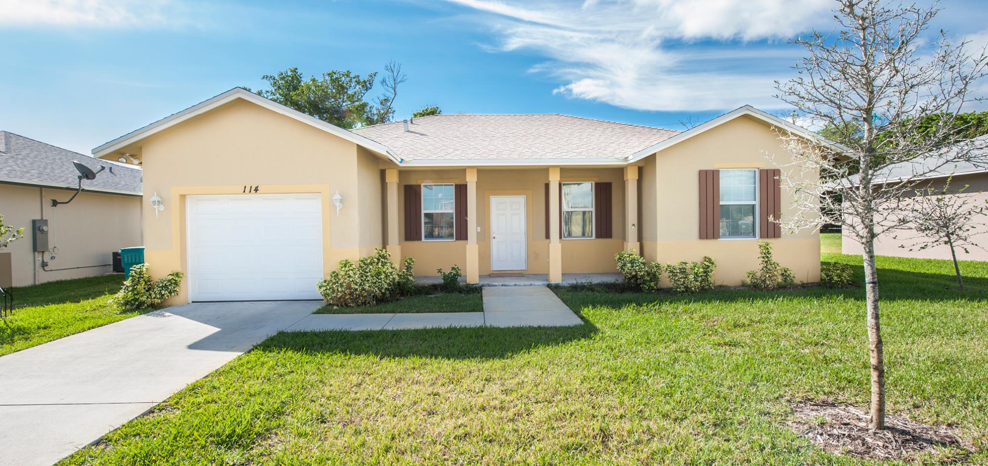 Yellow house with brown shutters, one story and one car garage with grass lawn