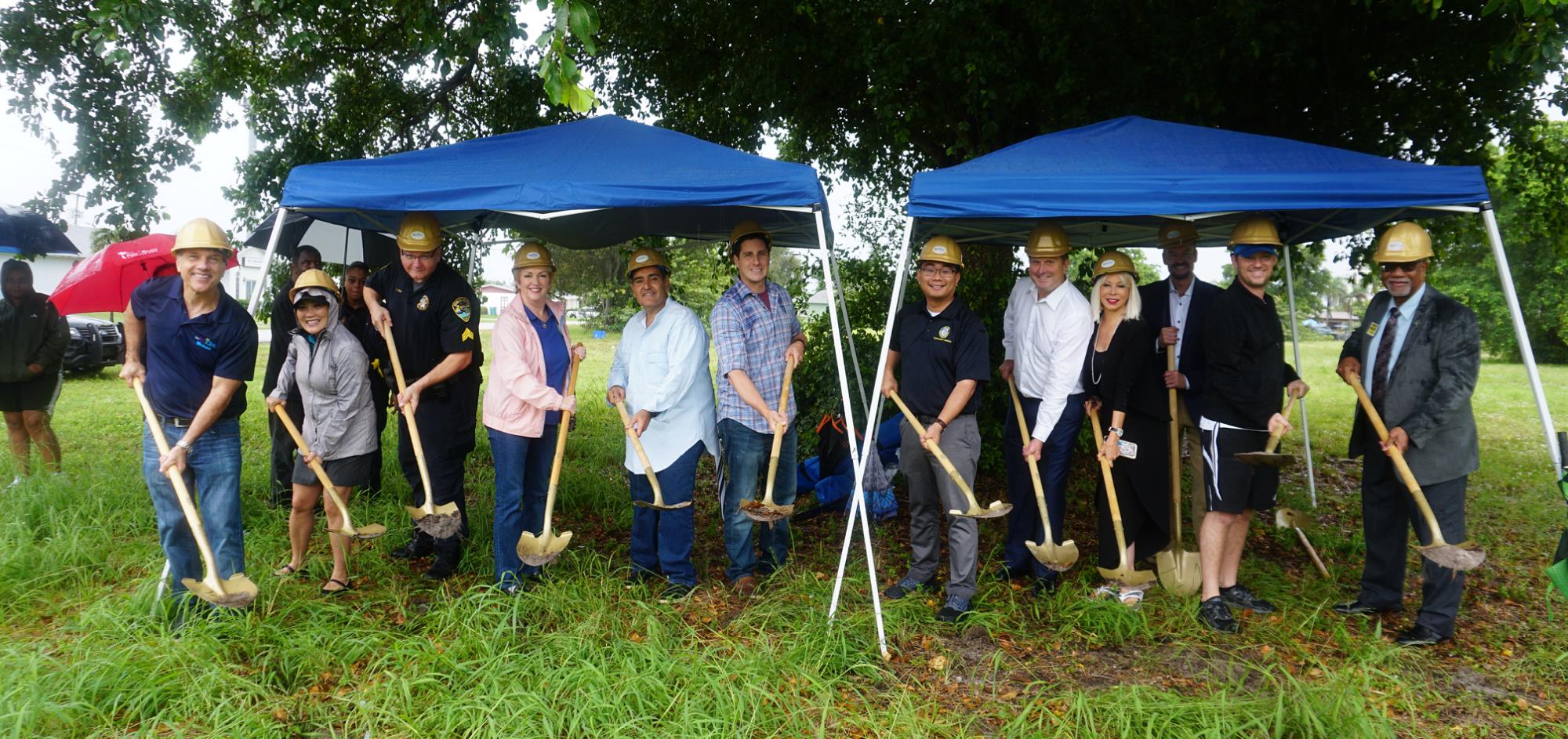 Groundbreaking group photo with City Commissioners, City Manager and Developers with shovels under blue tents in the rain